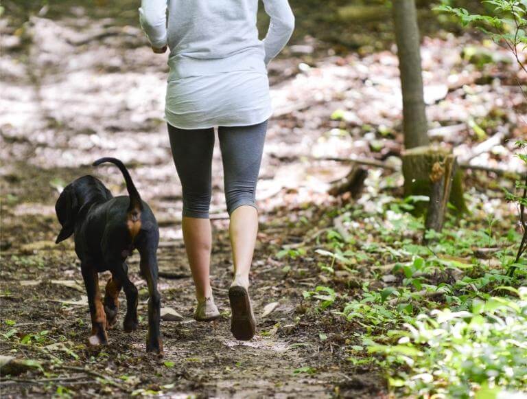 Kvinna som springer i skogen med en hund