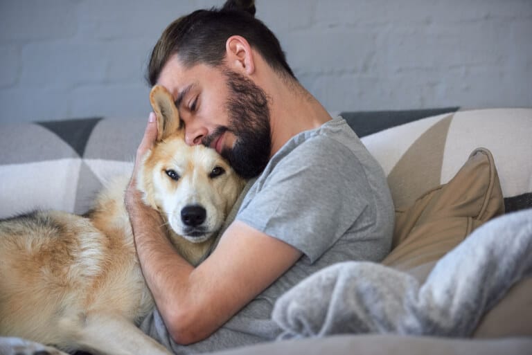 Man som kramar om sin hund i soffan