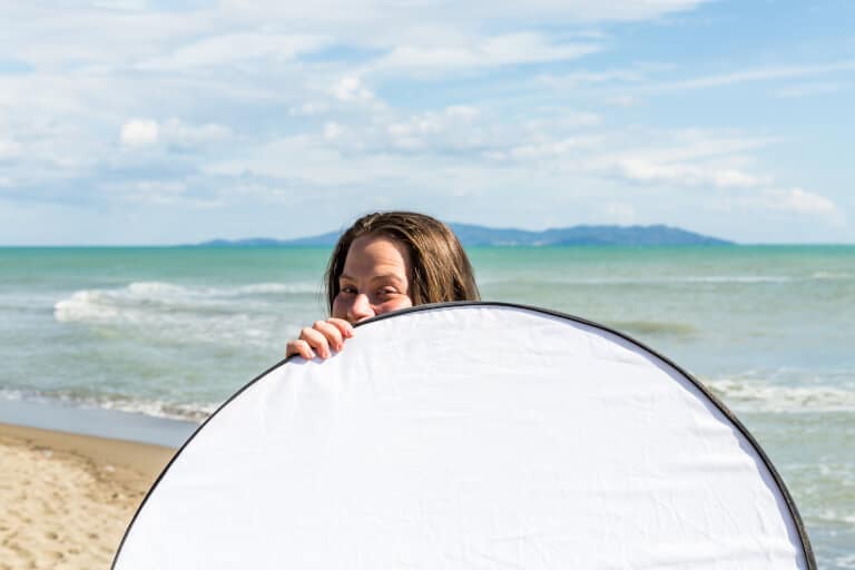 Kvinna som håller upp en reflexskärm på stranden
